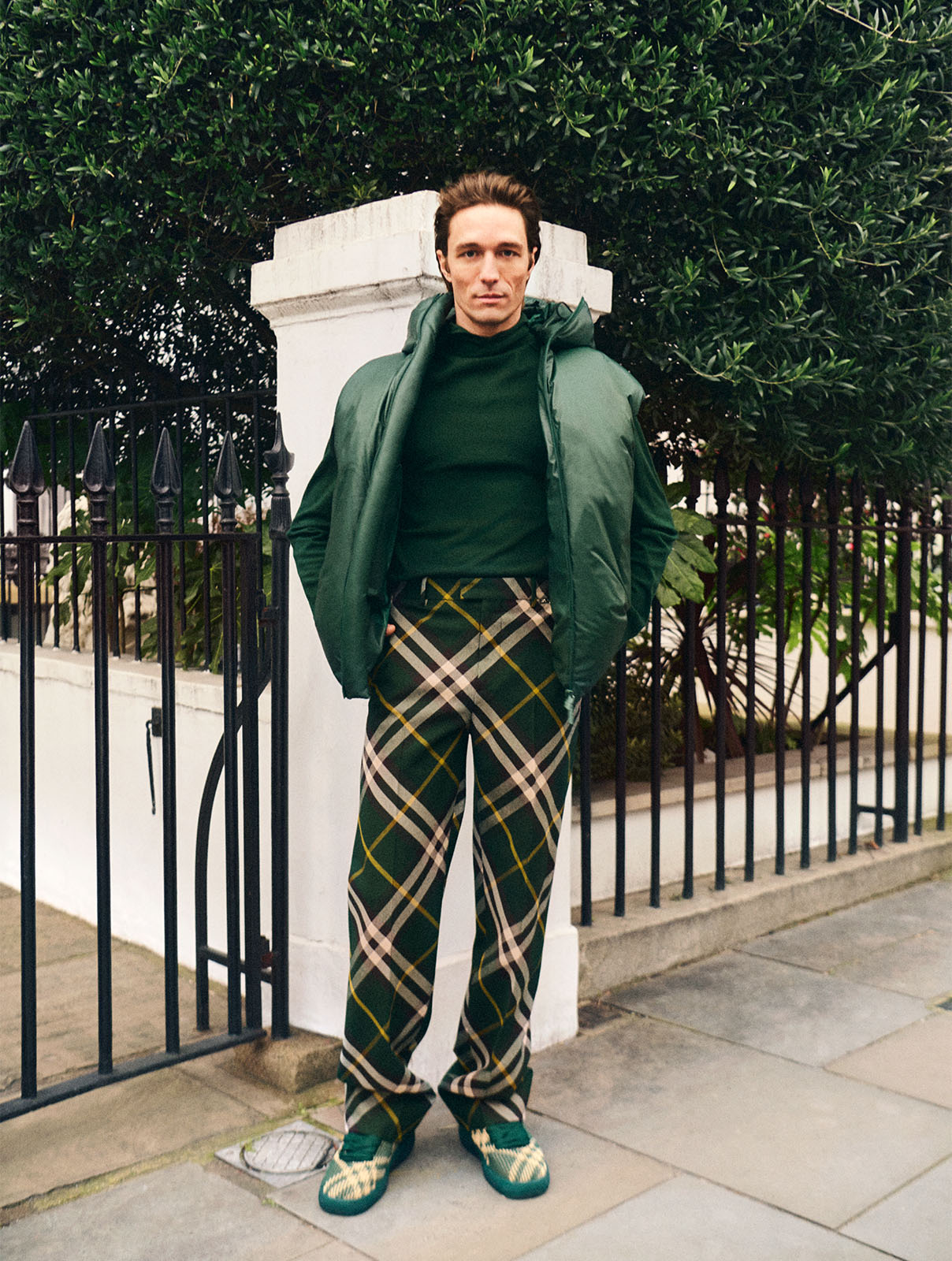 A male model wears a green Burberry puffer jacket and Burberry check trousers