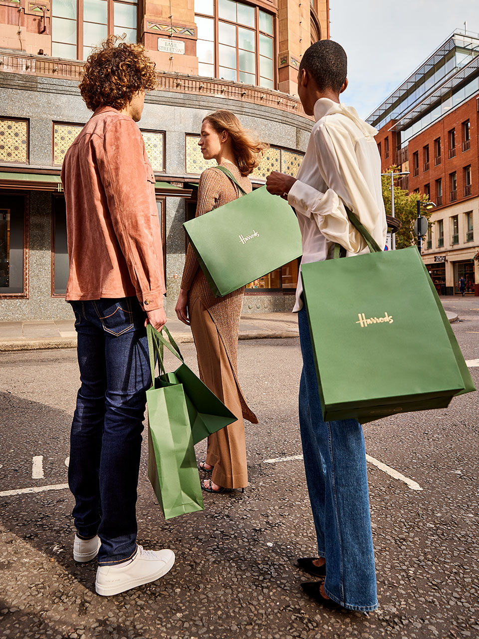 Group of friends standing outside the Harrods store holding icon green bag