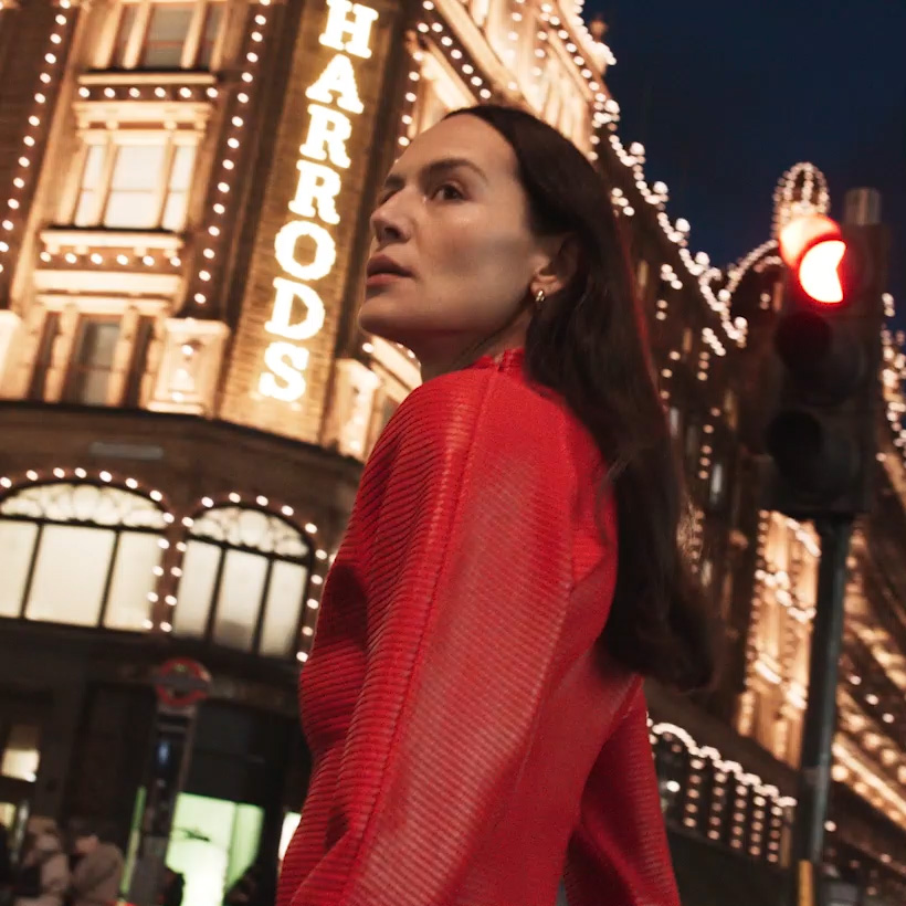 Woman in red walking outside Harrods at night